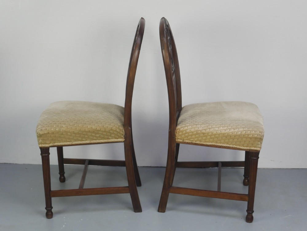 A pair of antique Georgian mahogany side chairs featuring pierced urn carved splats, arched backs, and upholstered seats supported by fluted front legs. View XXVIII