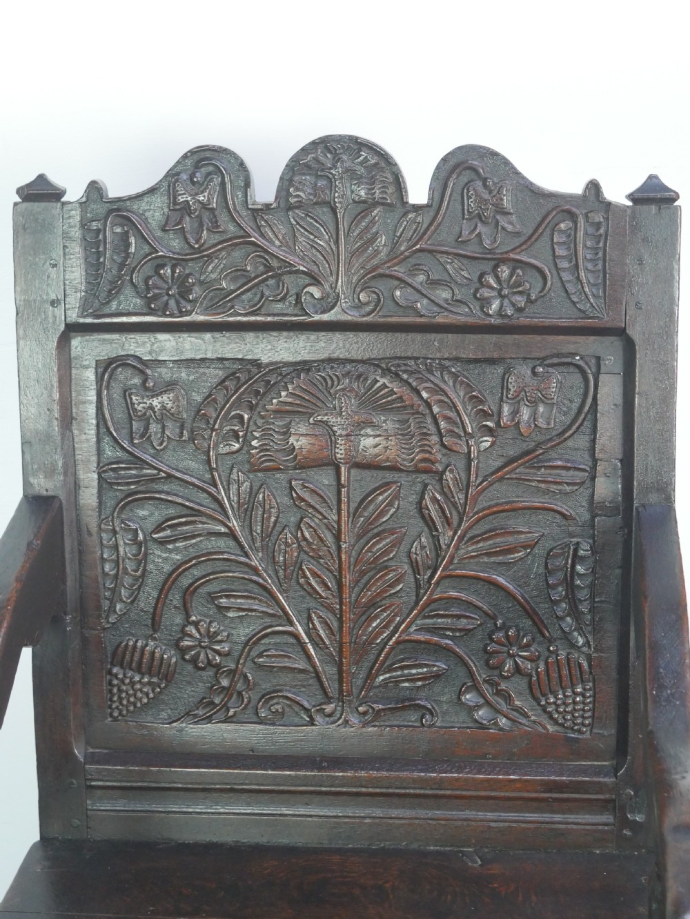 A dark oak 17th-century wainscot armchair featuring a relief-carved back panel, turned front legs, and flat armrests. View III