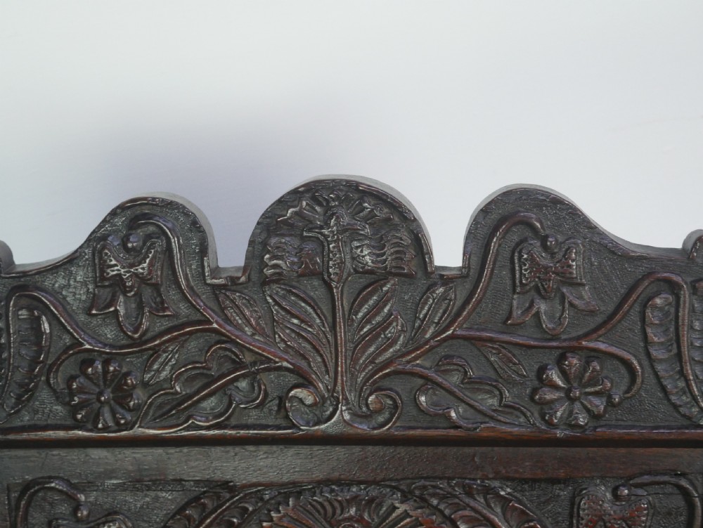 A dark oak 17th-century wainscot armchair featuring a relief-carved back panel, turned front legs, and flat armrests. View IV