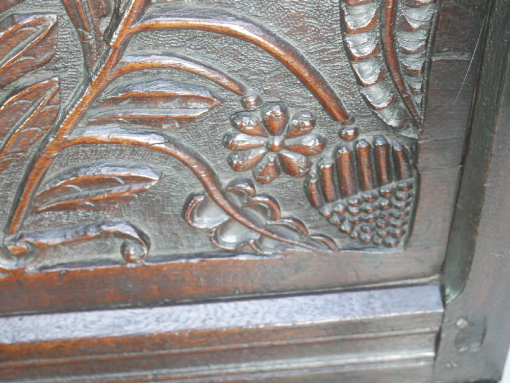 A dark oak 17th-century wainscot armchair featuring a relief-carved back panel, turned front legs, and flat armrests. View V