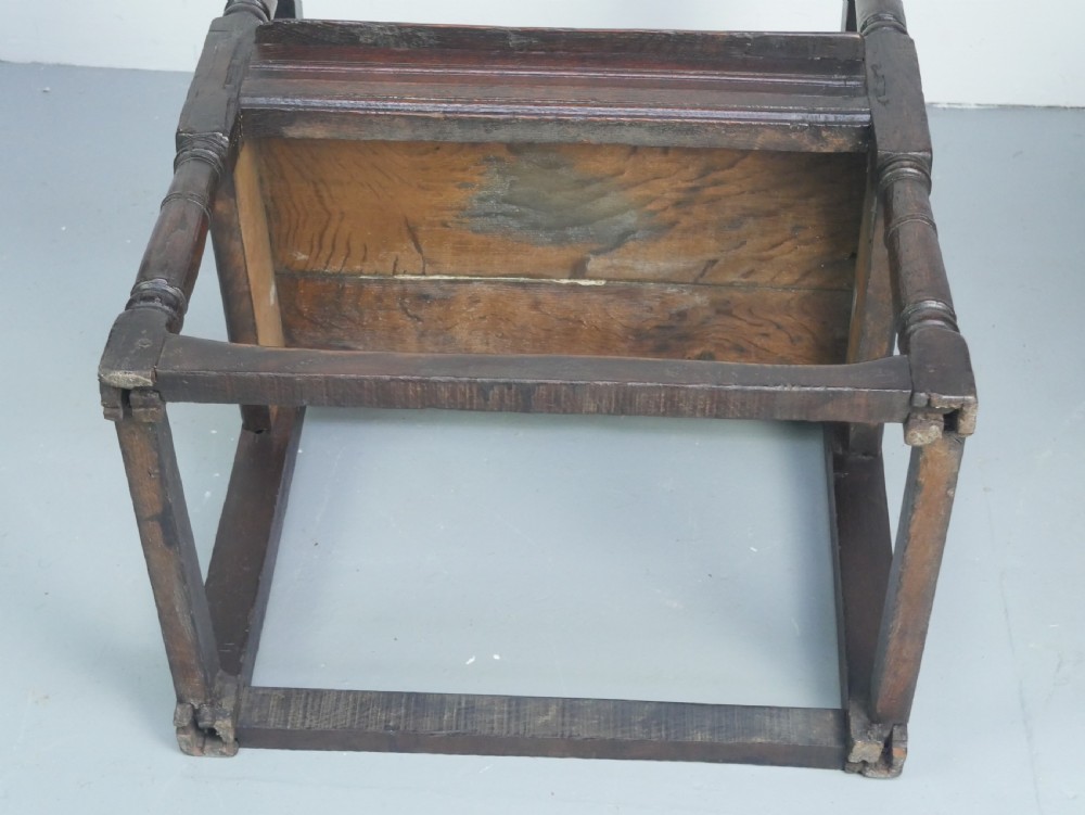A dark oak 17th-century wainscot armchair featuring a relief-carved back panel, turned front legs, and flat armrests. View XIII