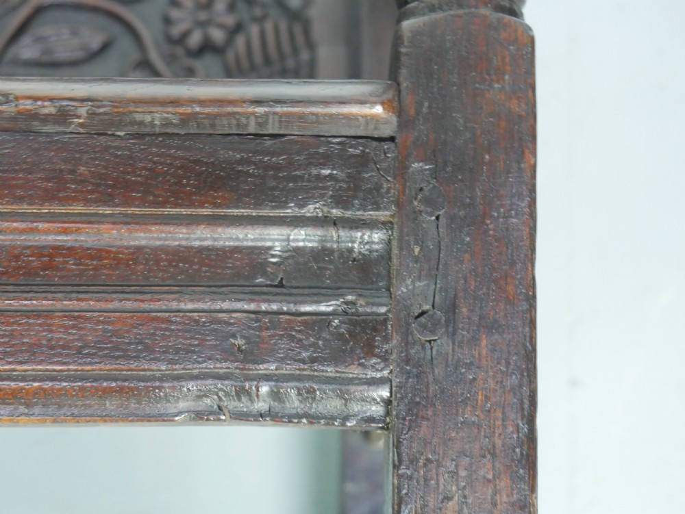 A dark oak 17th-century wainscot armchair featuring a relief-carved back panel, turned front legs, and flat armrests. View XVII