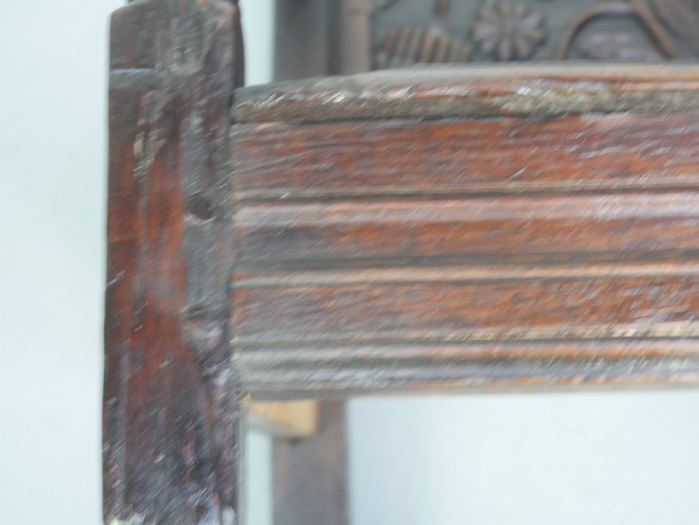 A dark oak 17th-century wainscot armchair featuring a relief-carved back panel, turned front legs, and flat armrests. View XVIII