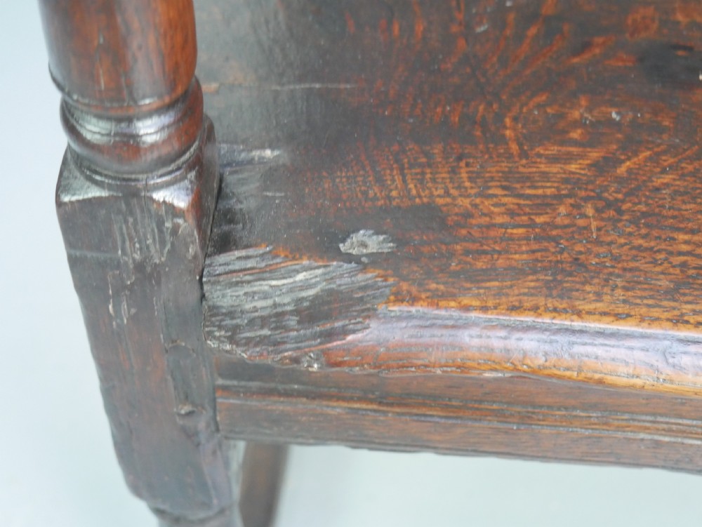 A dark oak 17th-century wainscot armchair featuring a relief-carved back panel, turned front legs, and flat armrests. View XXI