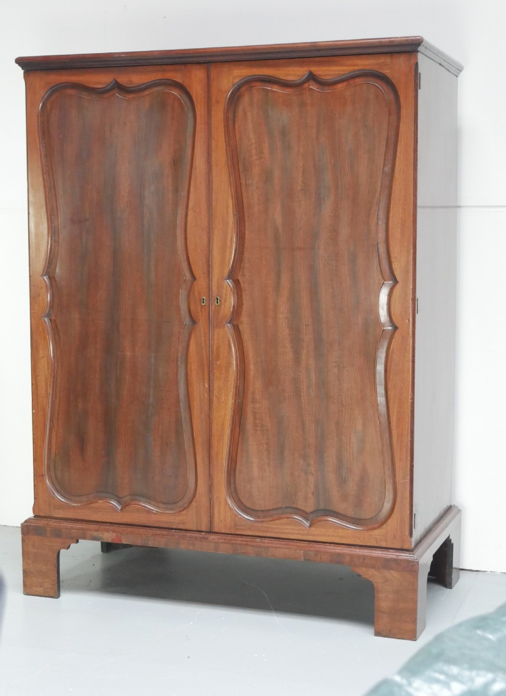 A Georgian mahogany double-door hanging wardrobe featuring shaped curvilinear door panels and sturdy bracket feet. View II