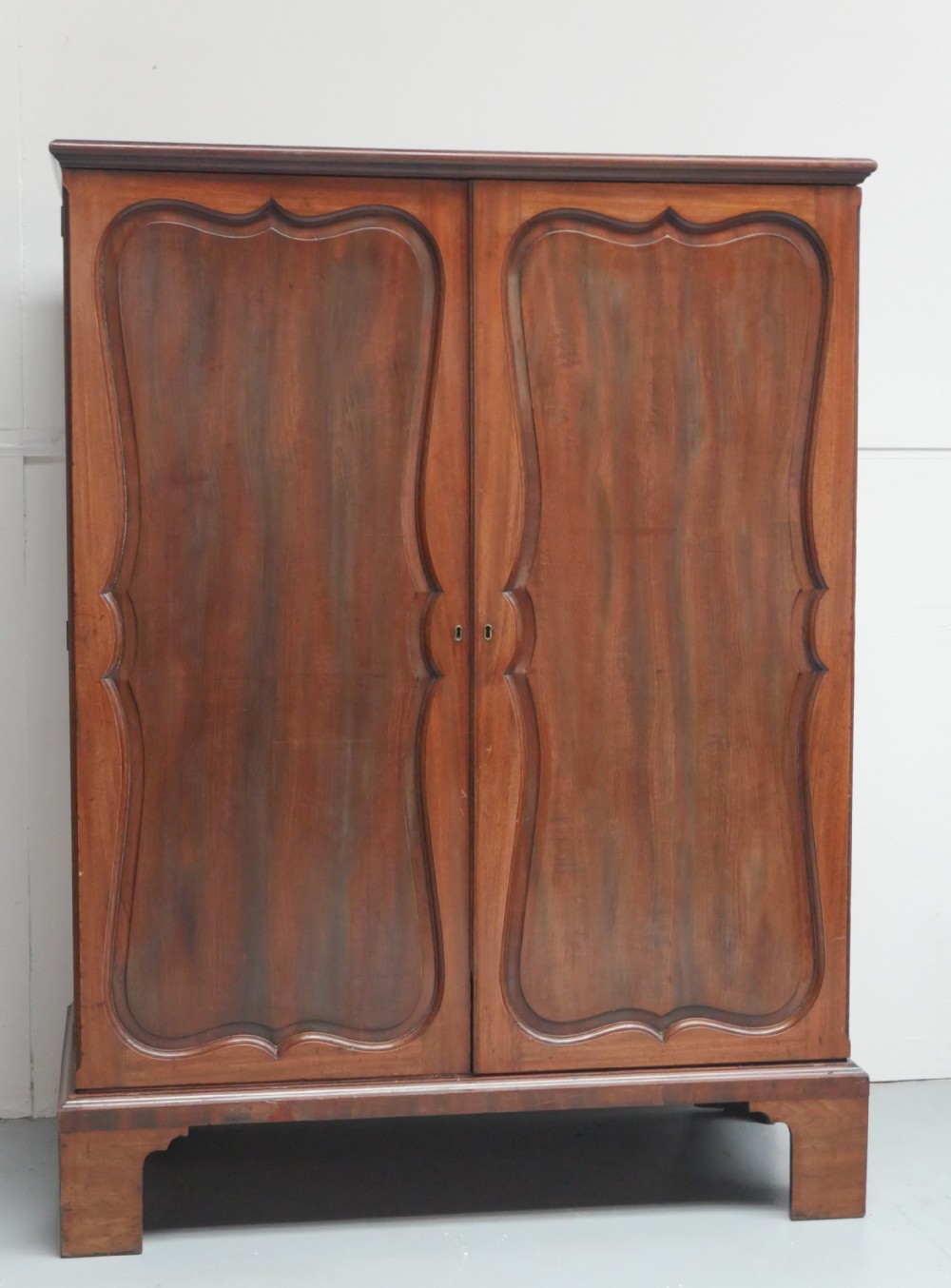A Georgian mahogany double-door hanging wardrobe featuring shaped curvilinear door panels and sturdy bracket feet. View XII
