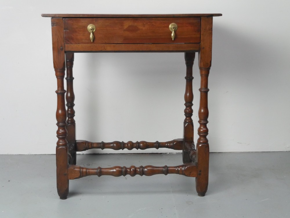 An 18th-century fruitwood side table featuring a single drawer with two brass teardrop handles, slender turned legs, and lower connecting stretchers.