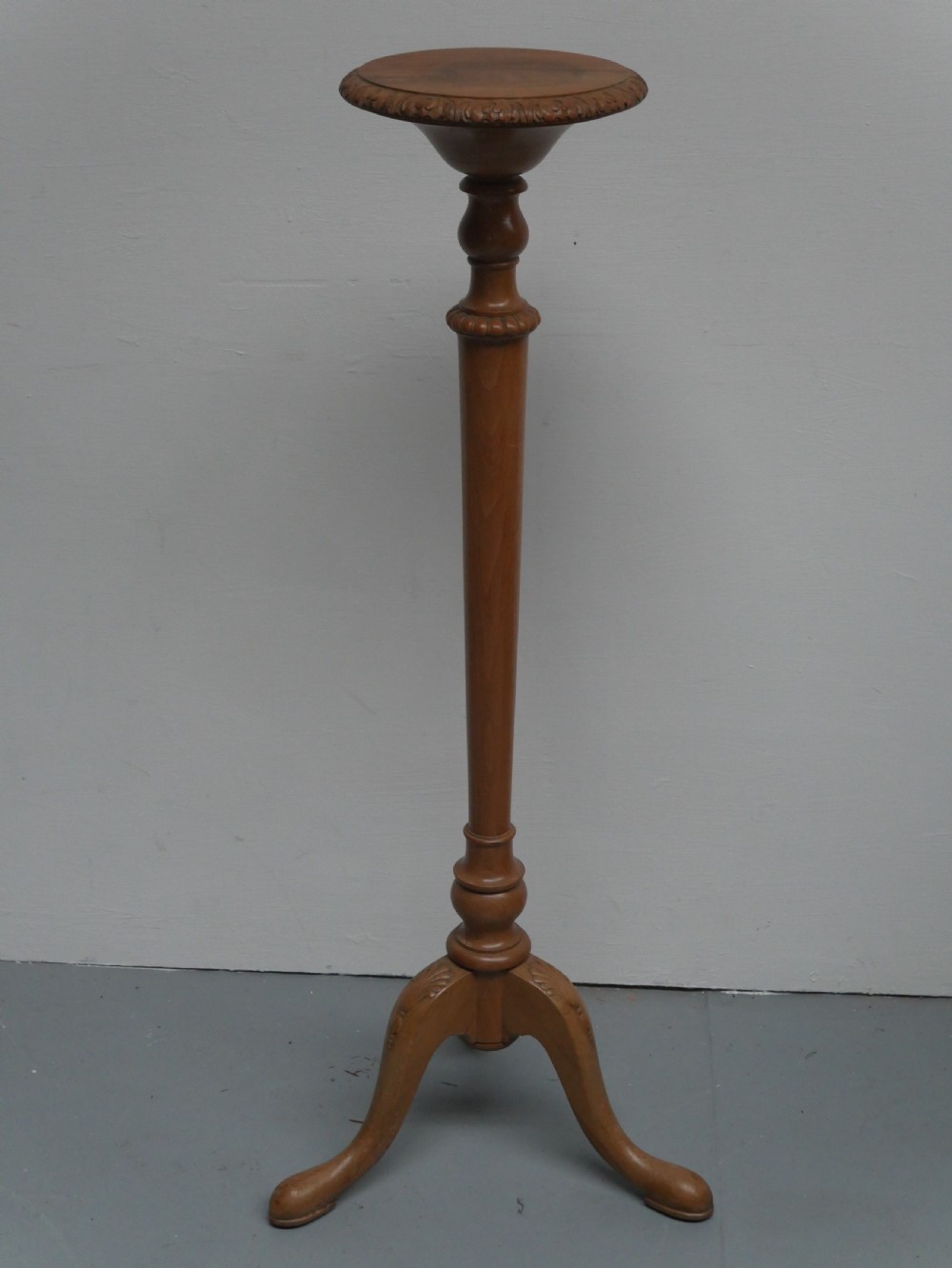A tall walnut plant stand featuring a carved circular top, turned central column, and tripod base with cabriole legs.