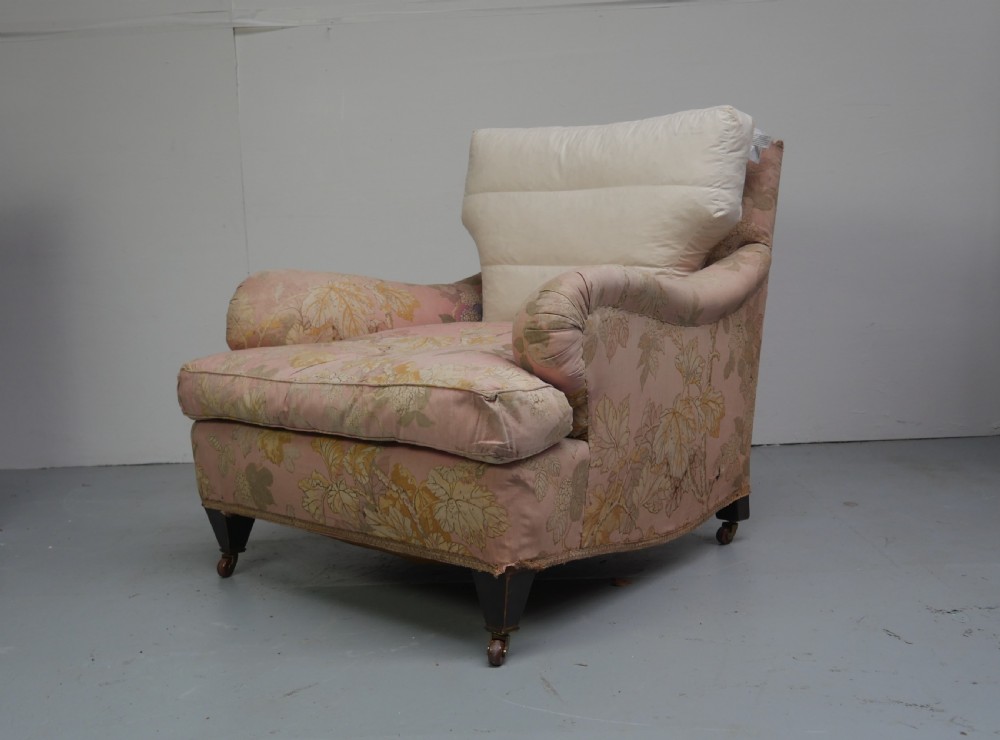 A Howard style deep seated armchair featuring pink floral pattern fabric, low rolled arms, and legs set on brass casters.