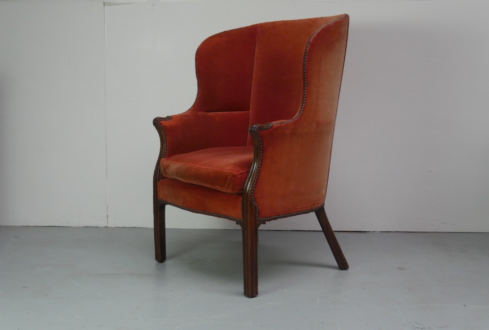 A Georgian high-backed barrel armchair upholstered in burnt orange velvet with brass stud trimming and dark mahogany legs.