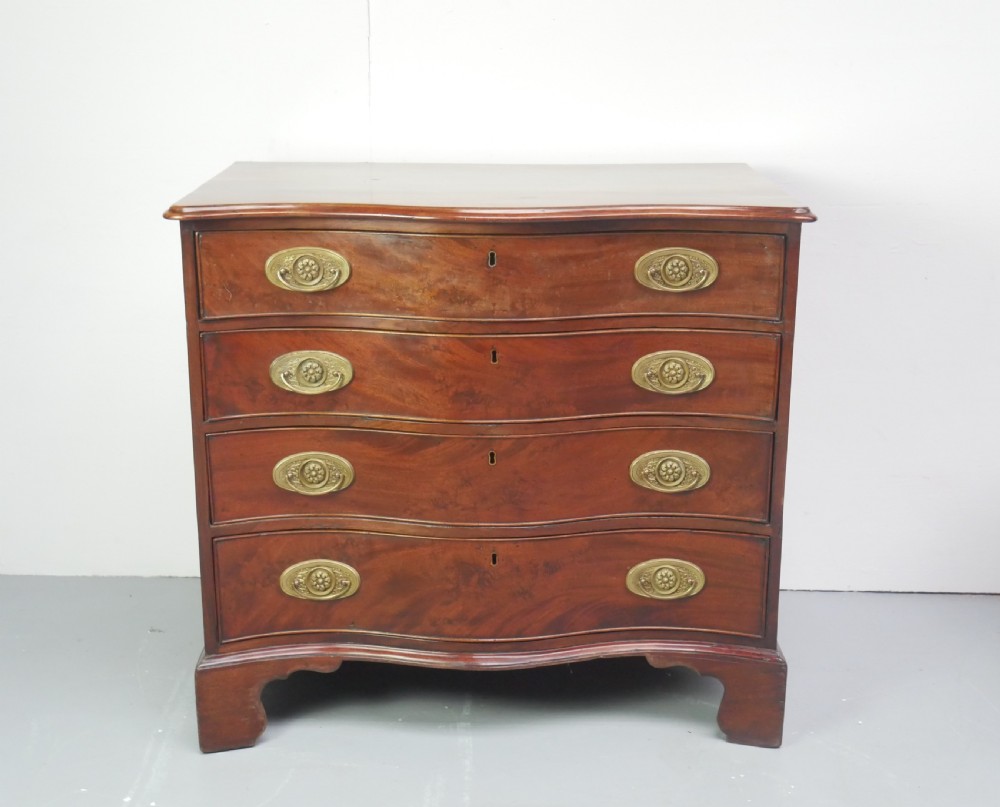A Georgian mahogany chest of drawers featuring a wave-like serpentine front, four graduated drawers with oval brass handles, and bracket feet.