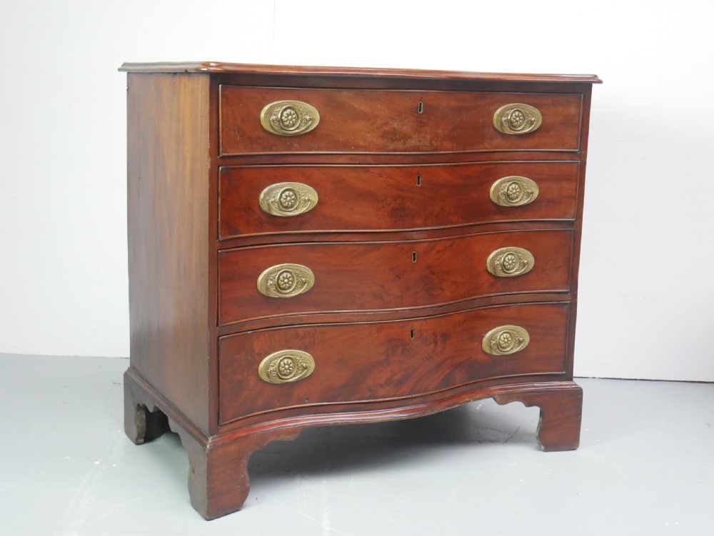 A Georgian mahogany chest of drawers featuring a wave-like serpentine front, four graduated drawers with oval brass handles, and bracket feet. View II