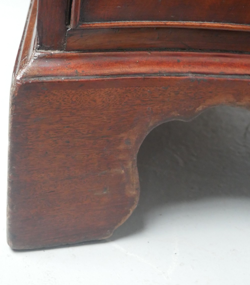 A Georgian mahogany chest of drawers featuring a wave-like serpentine front, four graduated drawers with oval brass handles, and bracket feet. View VII