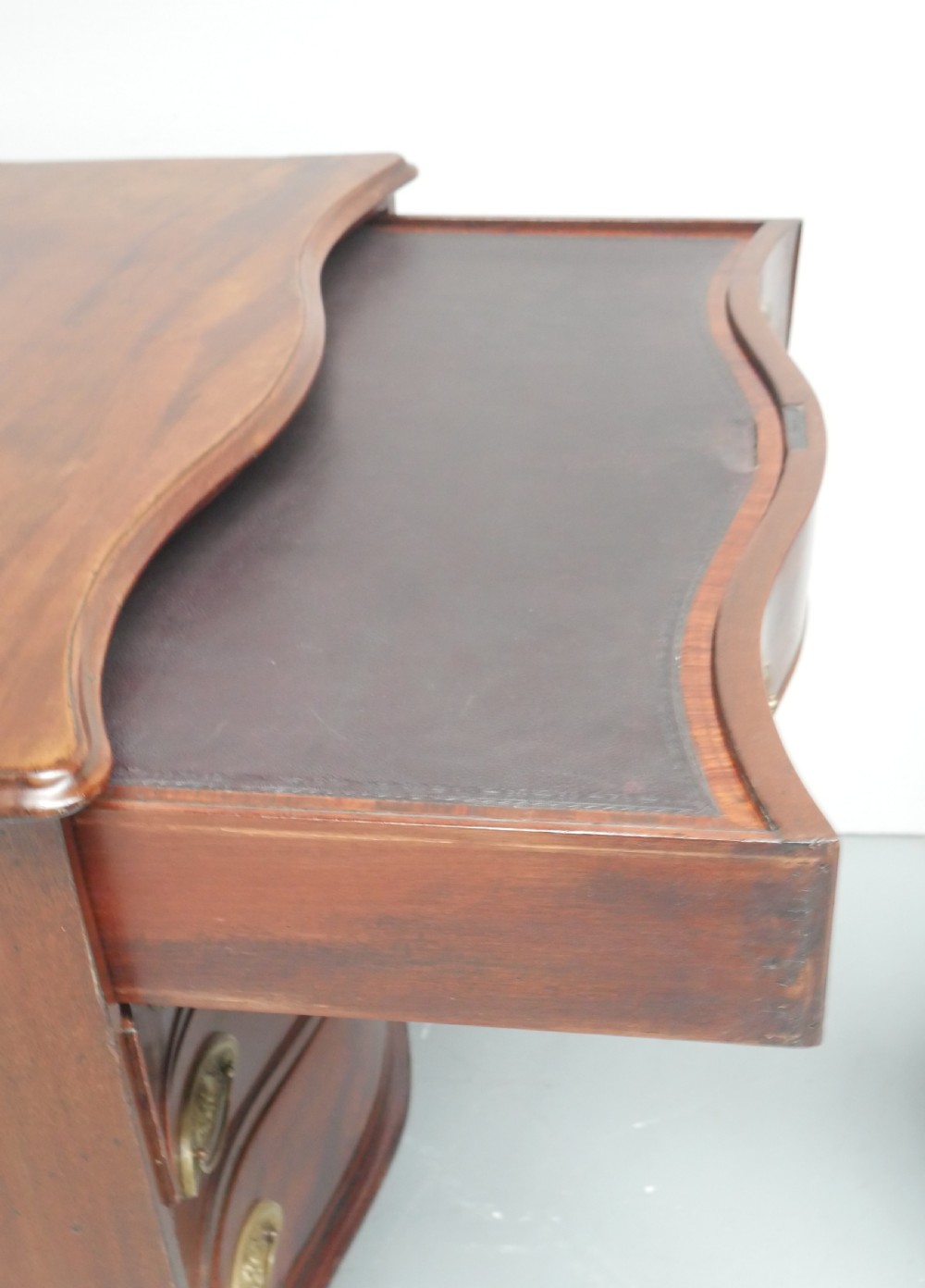 A Georgian mahogany chest of drawers featuring a wave-like serpentine front, four graduated drawers with oval brass handles, and bracket feet. View IX