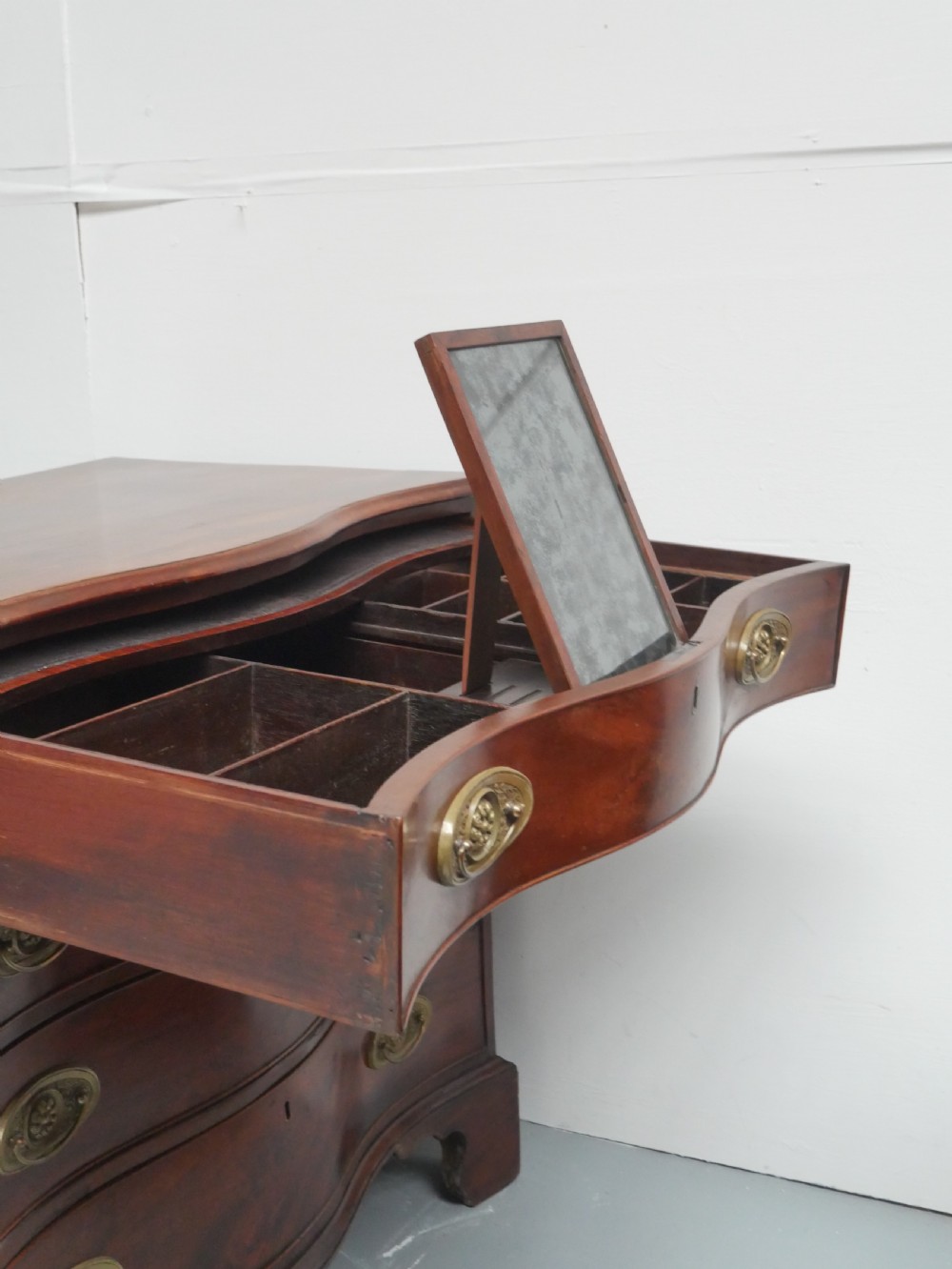 A Georgian mahogany chest of drawers featuring a wave-like serpentine front, four graduated drawers with oval brass handles, and bracket feet. View XIII