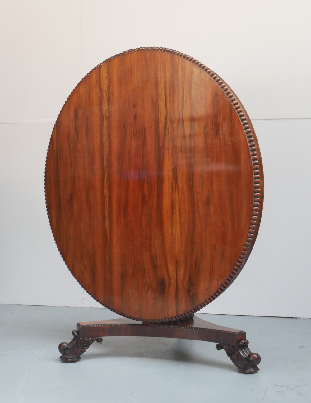 A Regency mahogany circular centre table featuring a beaded moulding edge, a carved gadrooned pedestal, and a triform base with scrolled feet. View II