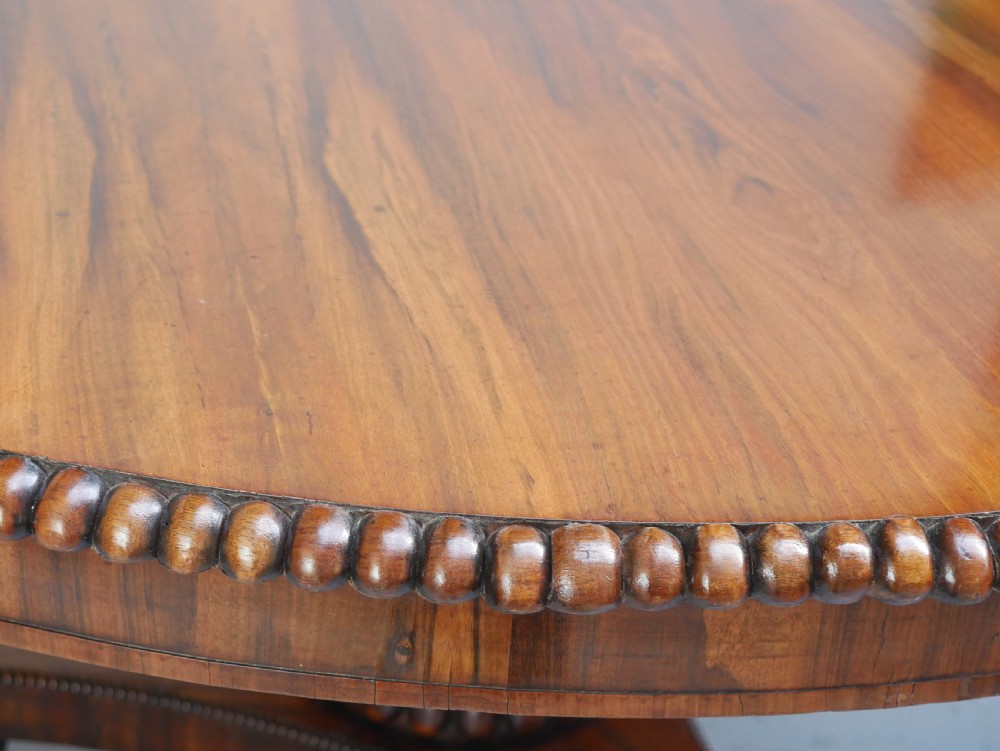 A Regency mahogany circular centre table featuring a beaded moulding edge, a carved gadrooned pedestal, and a triform base with scrolled feet. View V