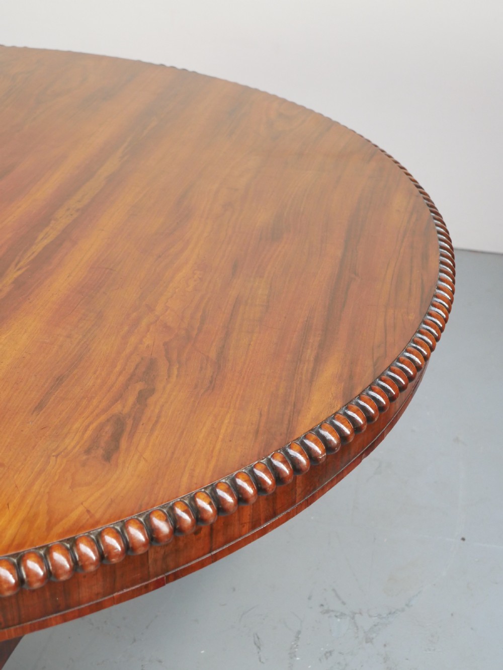 A Regency mahogany circular centre table featuring a beaded moulding edge, a carved gadrooned pedestal, and a triform base with scrolled feet. View VI