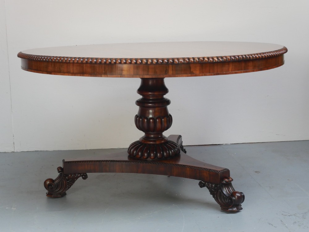 A Regency mahogany circular centre table featuring a beaded moulding edge, a carved gadrooned pedestal, and a triform base with scrolled feet. View X