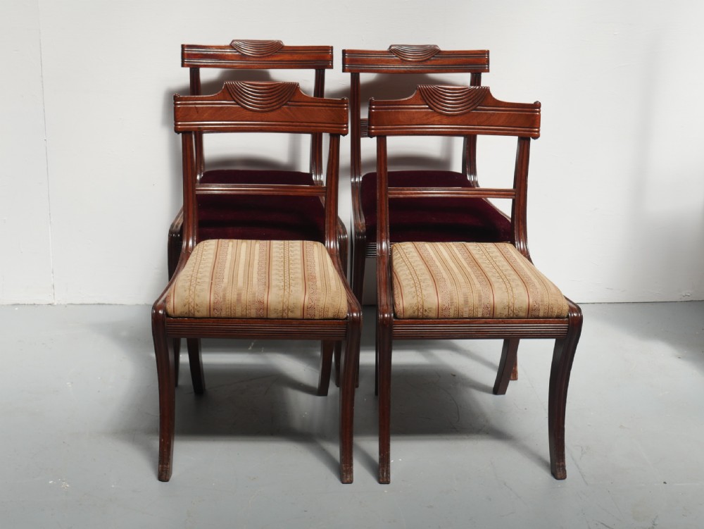 Set of four Regency mahogany dining chairs featuring carved crest rails, horizontal crossbars, and padded seats.