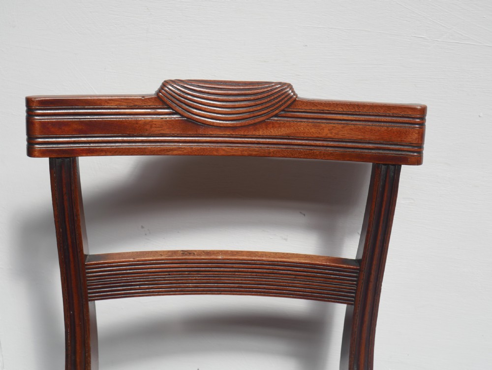 Set of four Regency mahogany dining chairs featuring carved crest rails, horizontal crossbars, and padded seats. View IV