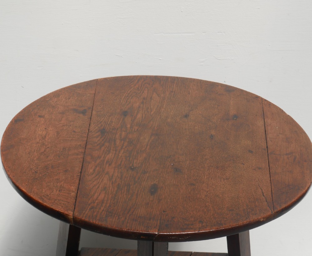A dark Georgian oak cricket table featuring a circular plank top, three tapered legs, and a lower triangular shelf. View II