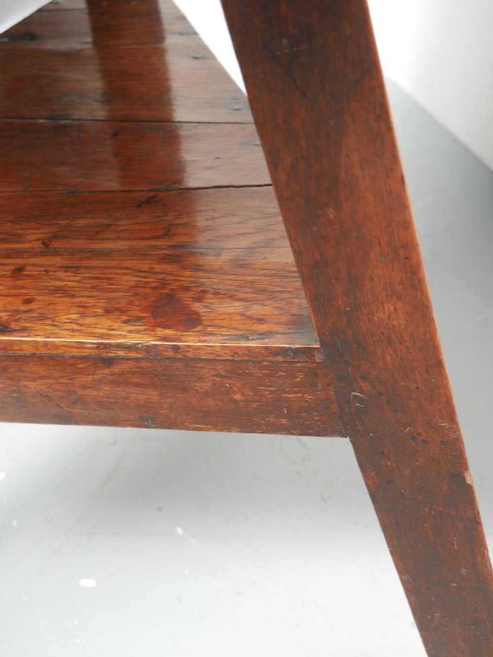A dark Georgian oak cricket table featuring a circular plank top, three tapered legs, and a lower triangular shelf. View VII