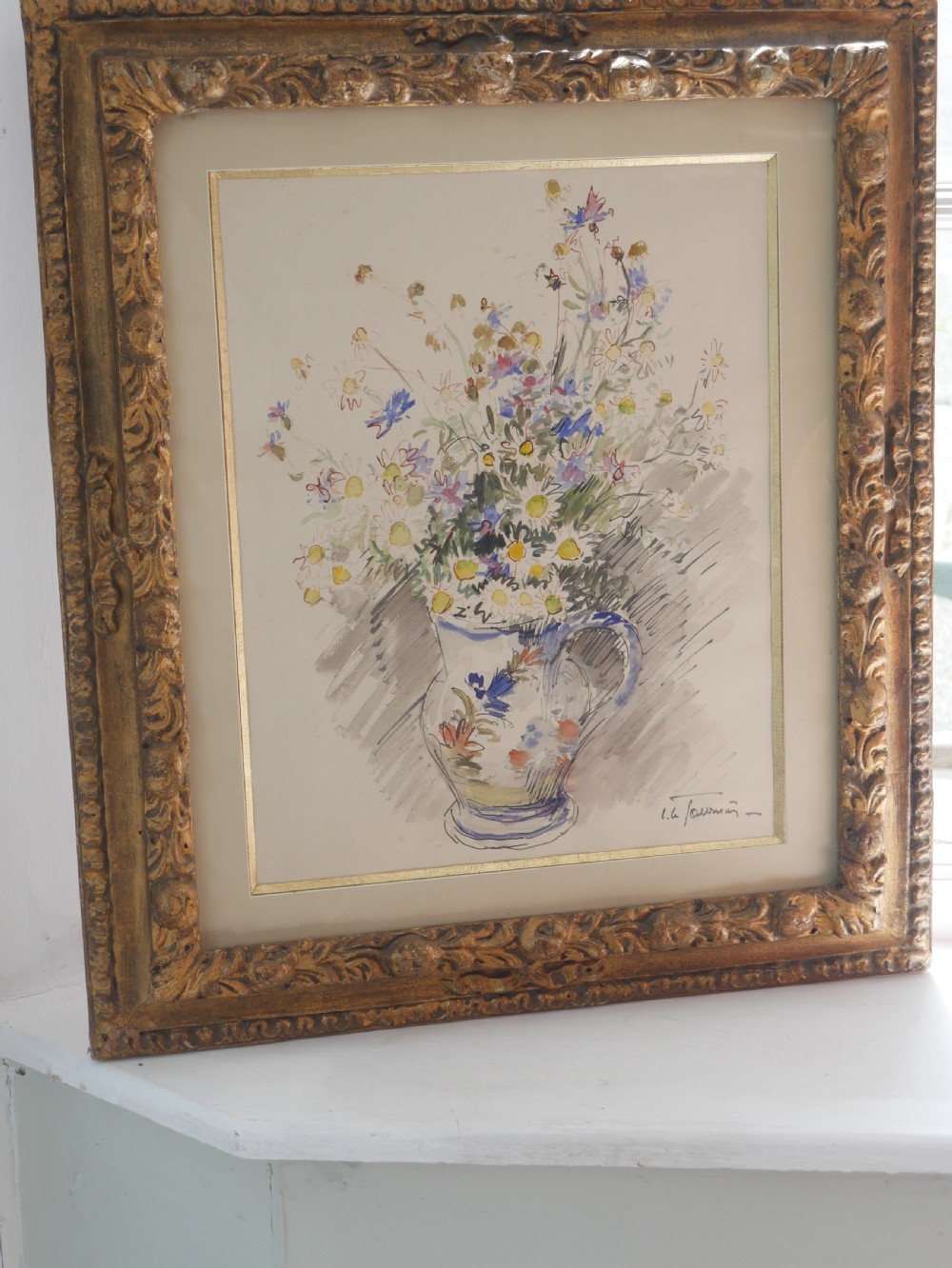 A framed floral watercolour still life painting depicting a bouquet of summer wildflowers in a ceramic jug within a carved giltwood frame.