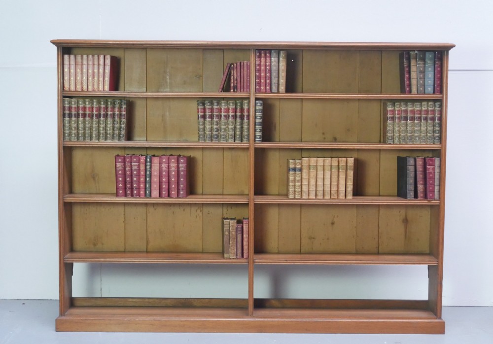 A large double-bay open oak bookcase with horizontal shelves filled with antique leather-bound books.