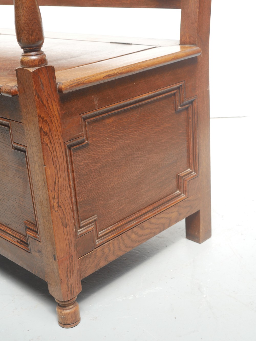 A medium brown oak hall bench featuring a tri-panel backrest, turned armrest supports, and a hinged lid chest base. View V
