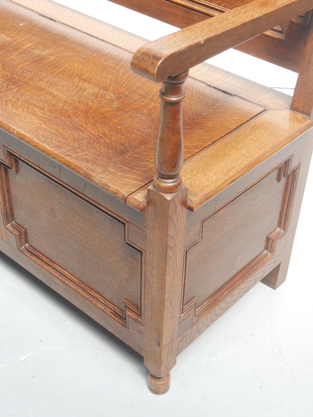 A medium brown oak hall bench featuring a tri-panel backrest, turned armrest supports, and a hinged lid chest base. View VI