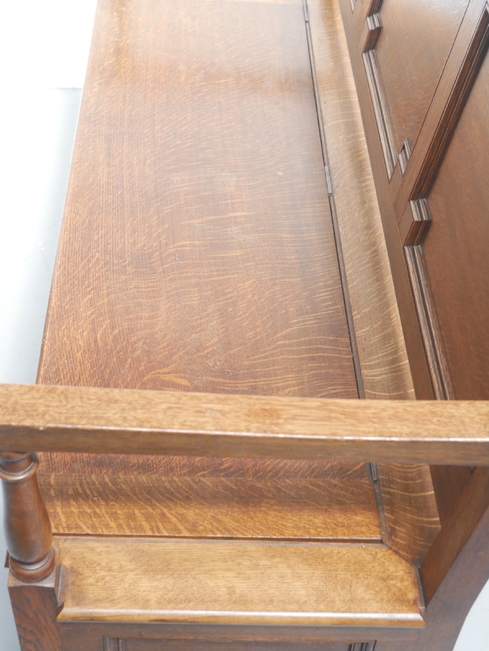 A medium brown oak hall bench featuring a tri-panel backrest, turned armrest supports, and a hinged lid chest base. View VII