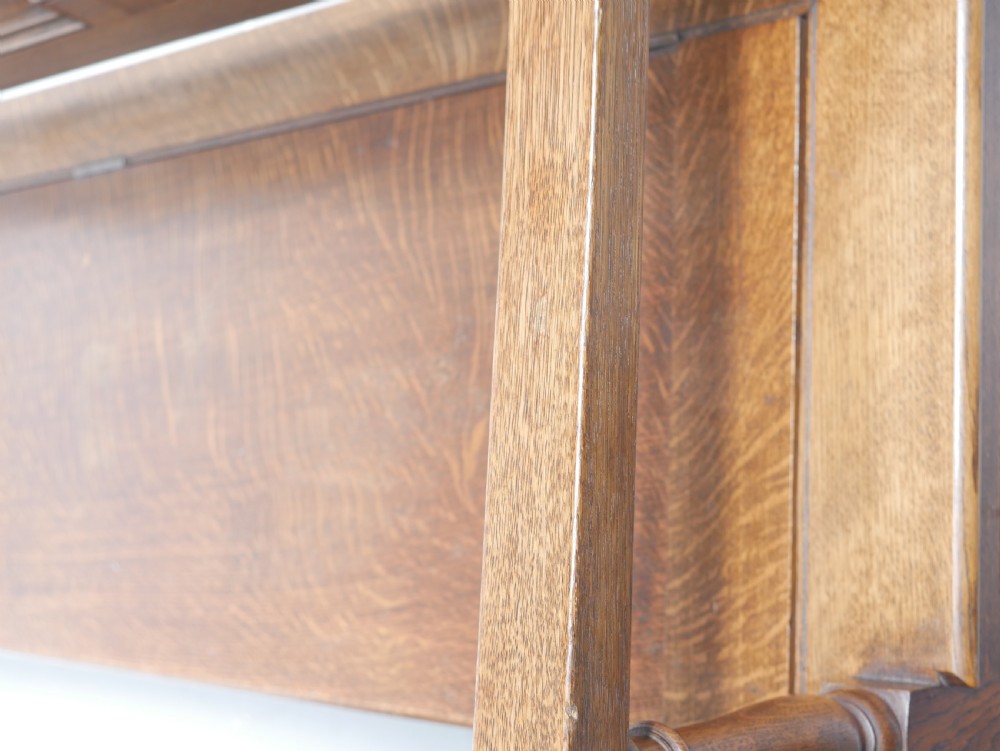 A medium brown oak hall bench featuring a tri-panel backrest, turned armrest supports, and a hinged lid chest base. View X