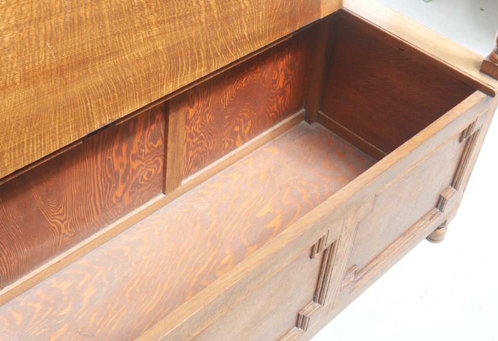 A medium brown oak hall bench featuring a tri-panel backrest, turned armrest supports, and a hinged lid chest base. View XIII