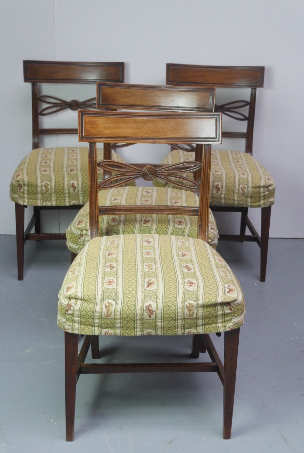 A set of four Scottish Georgian mahogany dining chairs featuring carved bow splats, square legs with stretchers, and green and cream patterned upholstery.