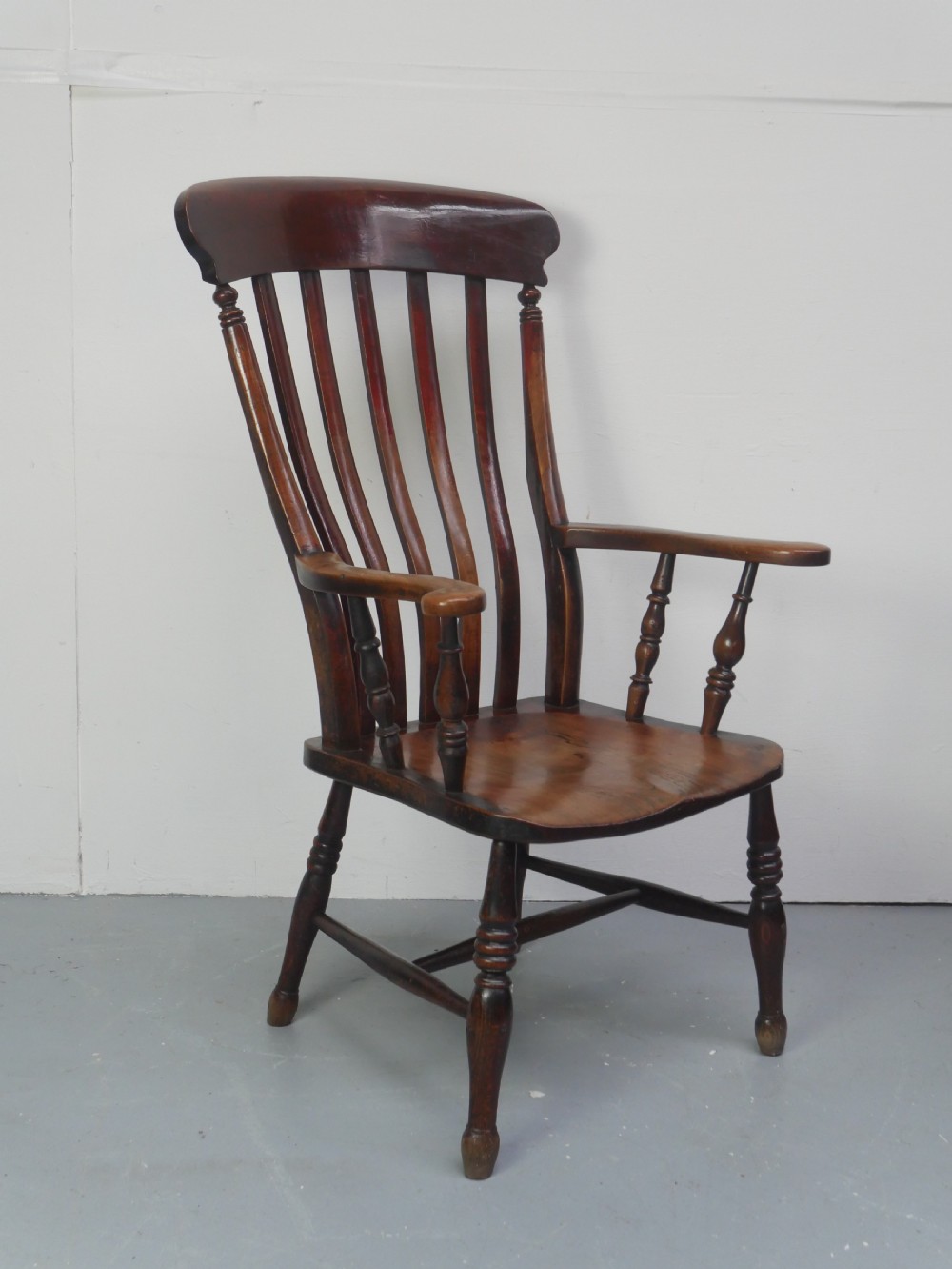 A dark brown wooden country armchair featuring a high spindle back, curved crest rail, shaped seat, and turned legs.