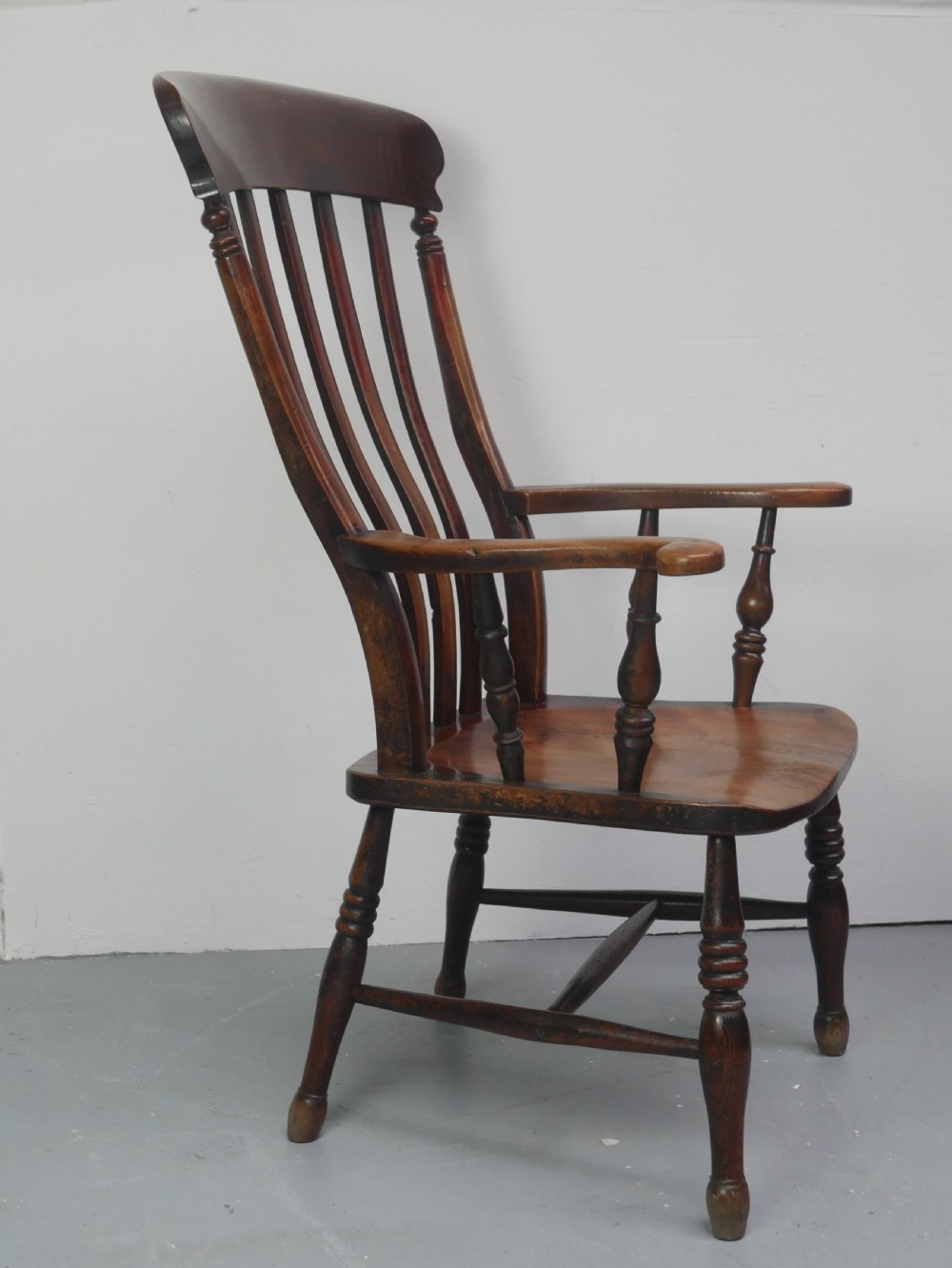 A dark brown wooden country armchair featuring a high spindle back, curved crest rail, shaped seat, and turned legs. View V