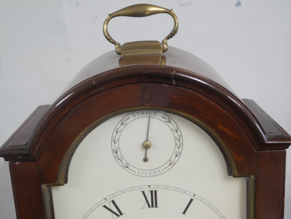 A Georgian mahogany bracket clock featuring an arched top with a brass handle, white dial with Roman numerals, and strike silent sub-dial. View VII