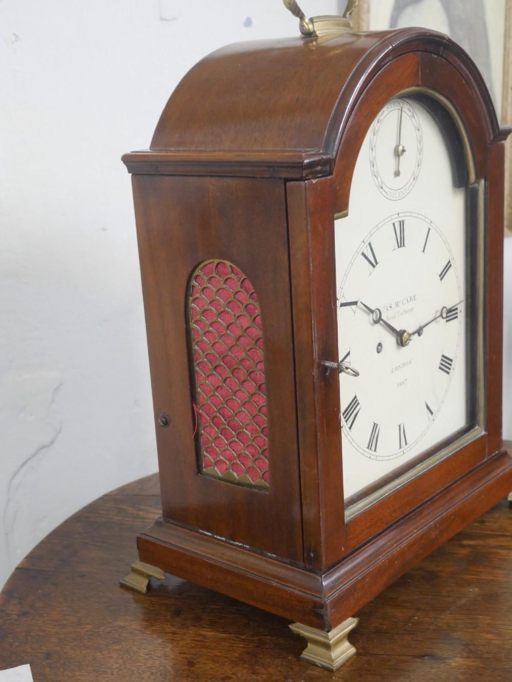 A Georgian mahogany bracket clock featuring an arched top with a brass handle, white dial with Roman numerals, and strike silent sub-dial. View IX