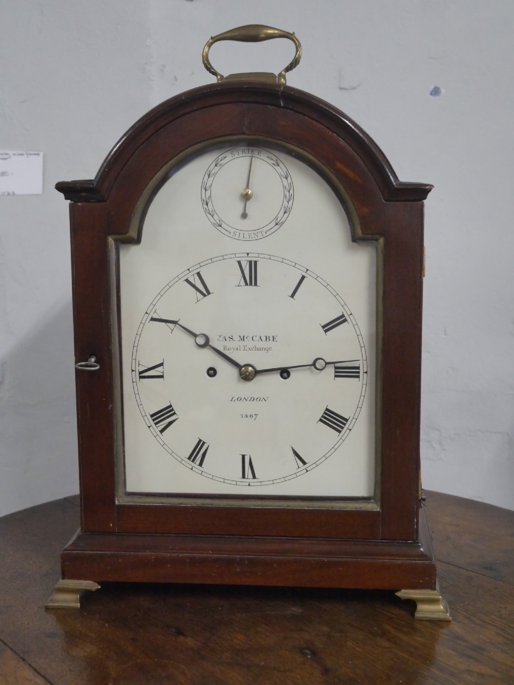 A Georgian mahogany bracket clock featuring an arched top with a brass handle, white dial with Roman numerals, and strike silent sub-dial. View XIII