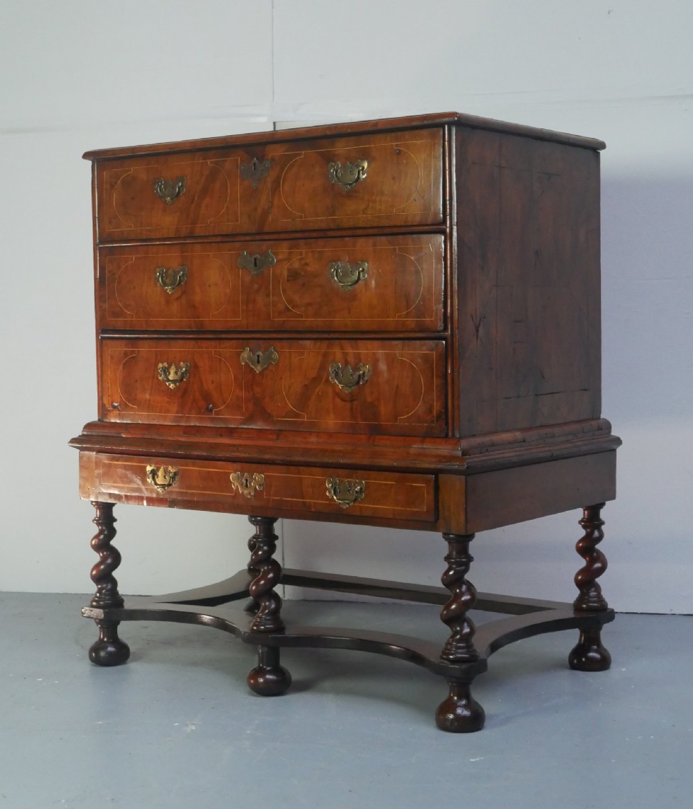 A late 17th-century William and Mary walnut chest on stand featuring multiple drawers with feather inlay, barley twist legs, and bun feet.