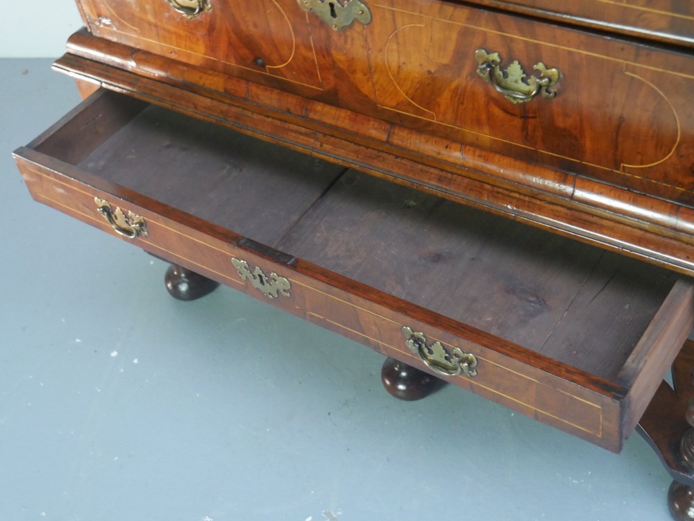 A late 17th-century William and Mary walnut chest on stand featuring multiple drawers with feather inlay, barley twist legs, and bun feet. View V