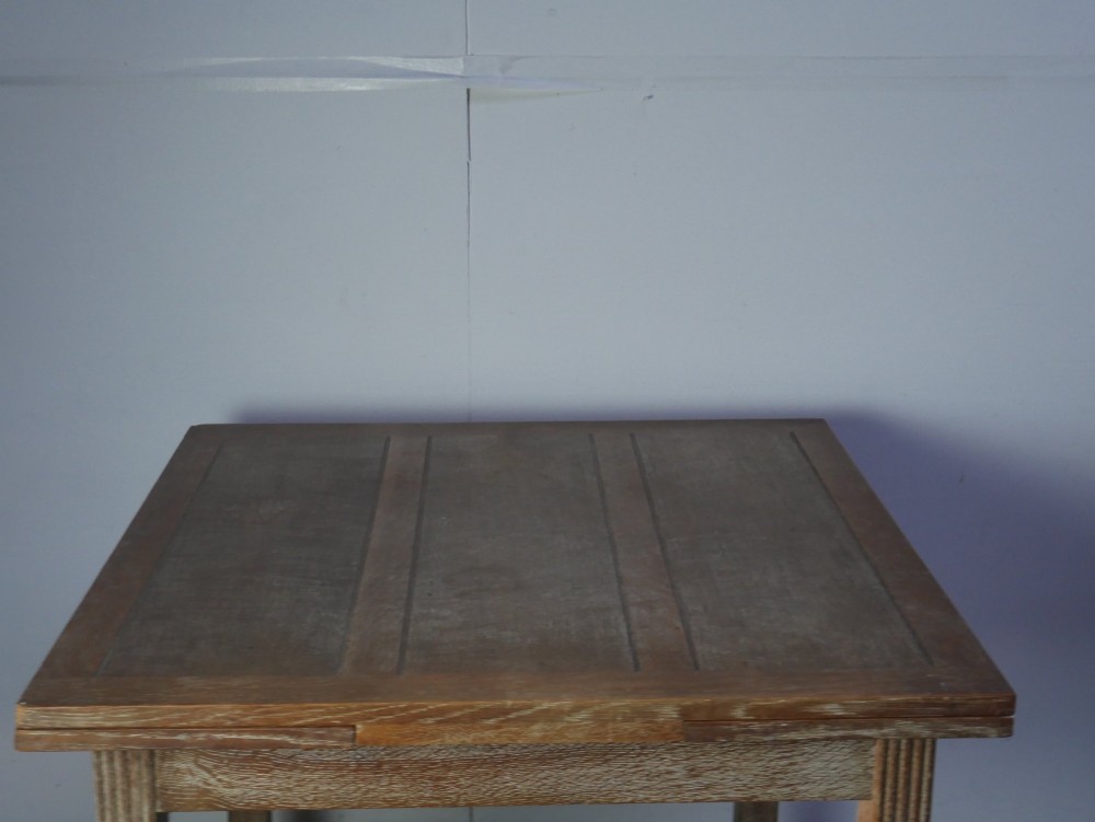 A square limed oak dining table featuring reeded legs, an X-shaped cross stretcher, and a draw-leaf top mechanism. View II