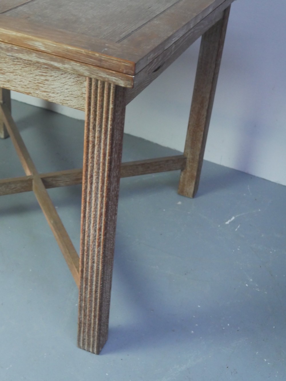 A square limed oak dining table featuring reeded legs, an X-shaped cross stretcher, and a draw-leaf top mechanism. View V