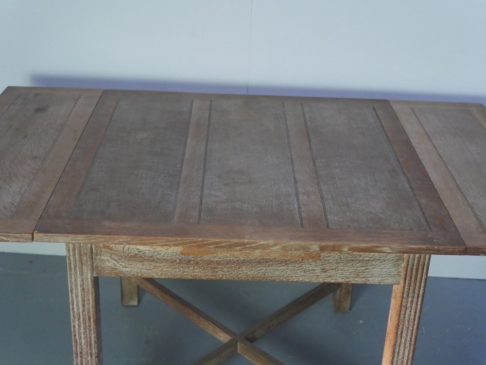 A square limed oak dining table featuring reeded legs, an X-shaped cross stretcher, and a draw-leaf top mechanism. View VIII
