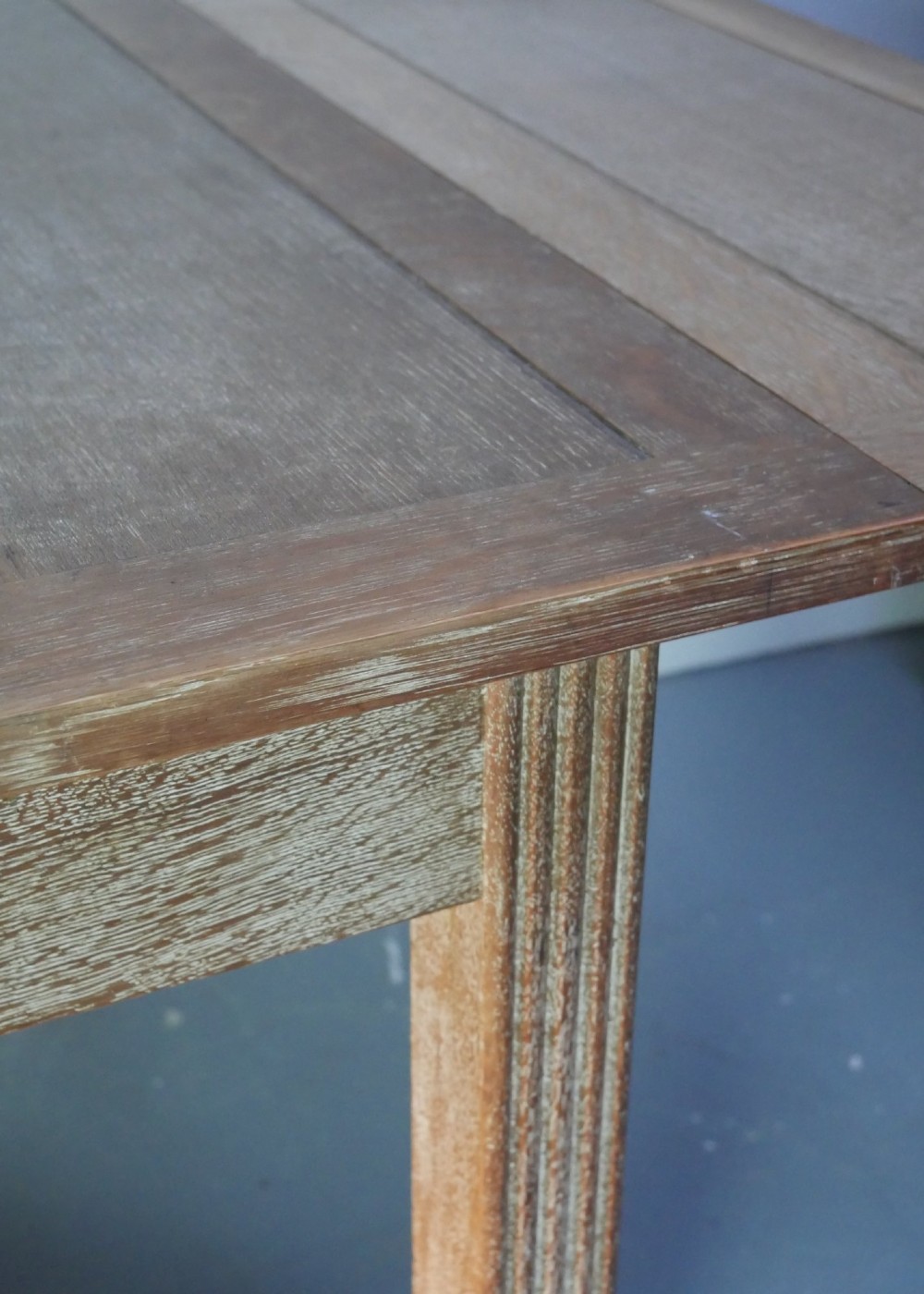 A square limed oak dining table featuring reeded legs, an X-shaped cross stretcher, and a draw-leaf top mechanism. View X