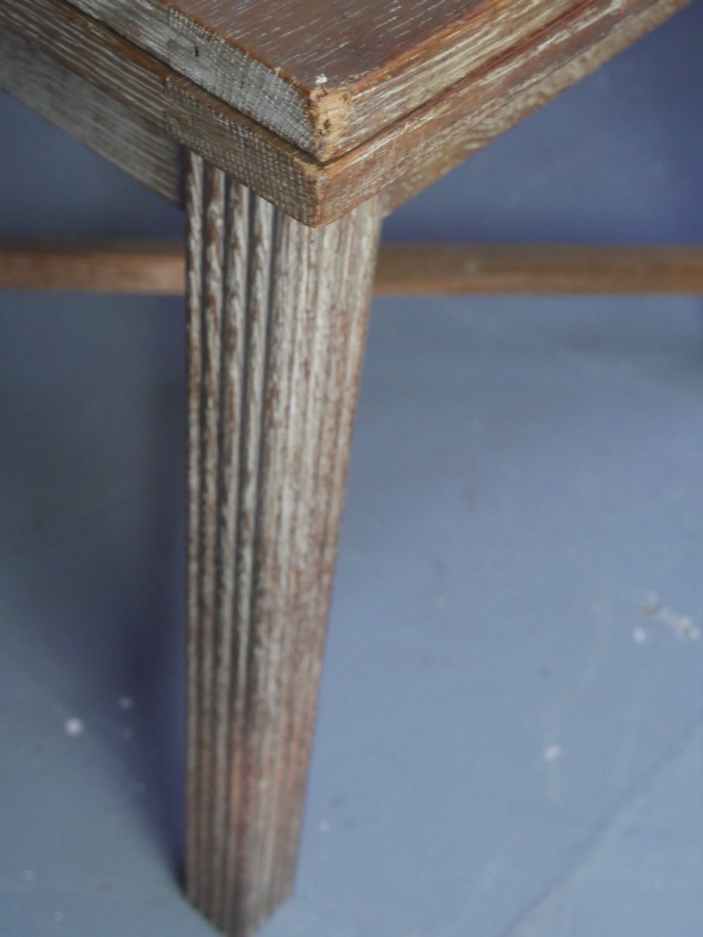 A square limed oak dining table featuring reeded legs, an X-shaped cross stretcher, and a draw-leaf top mechanism. View VI