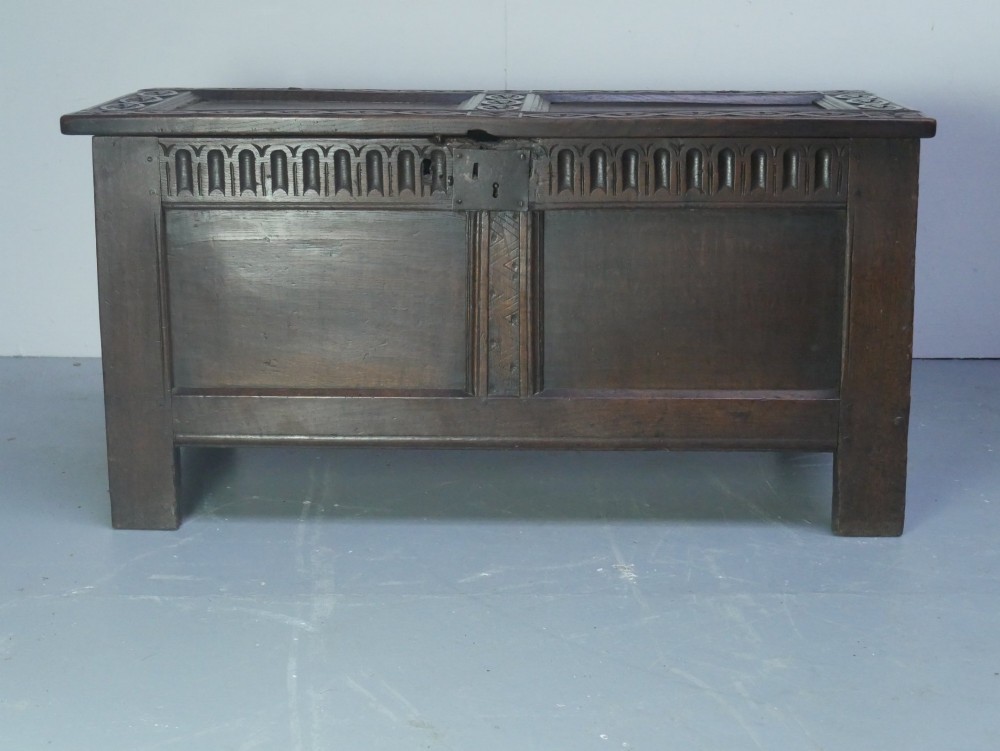 A dark brown oak coffer featuring a carved fluted frieze, double front panels, and a hinged lid with carved geometric border details.