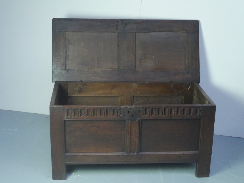 A dark brown oak coffer featuring a carved fluted frieze, double front panels, and a hinged lid with carved geometric border details. View II