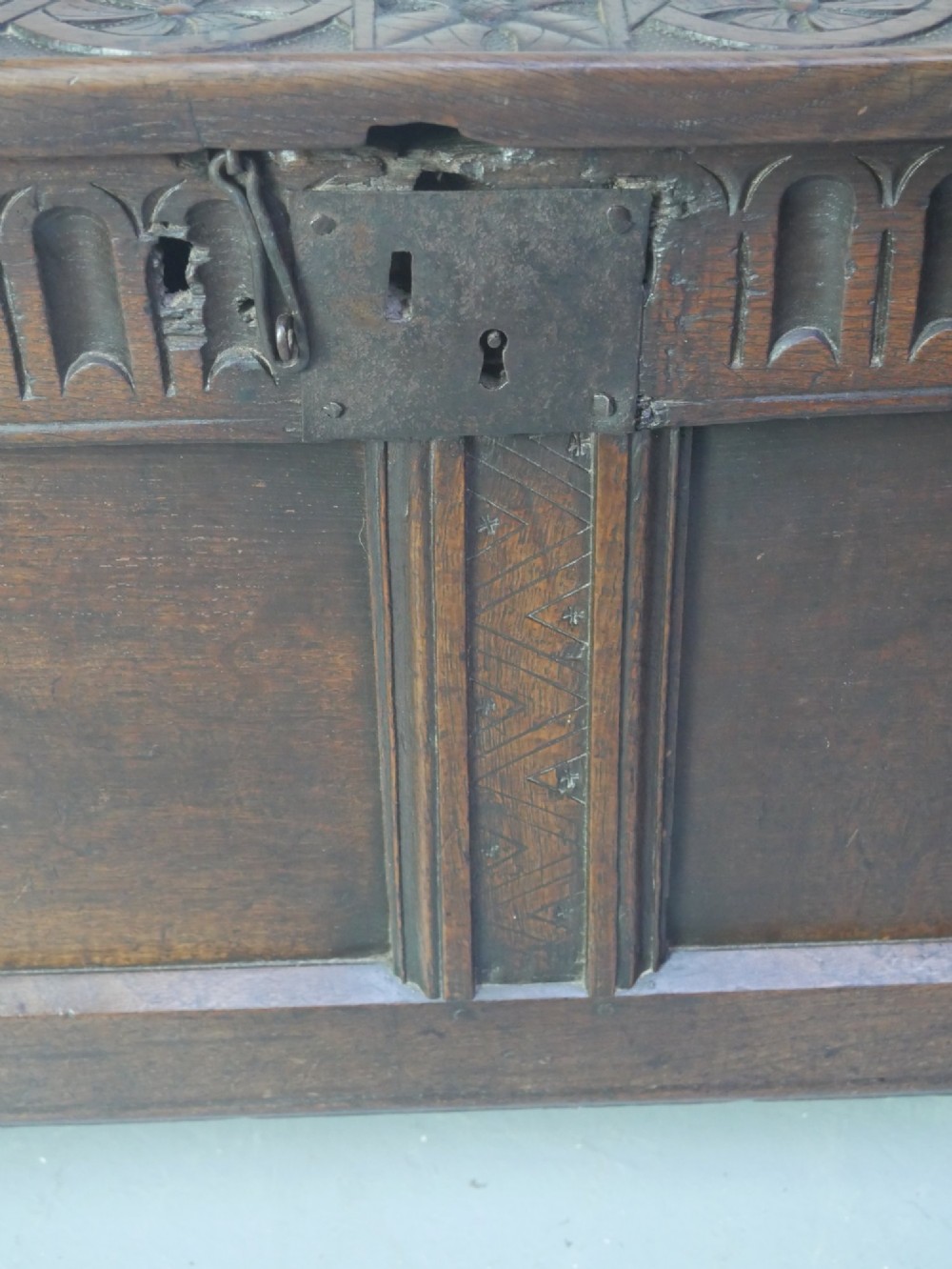 A dark brown oak coffer featuring a carved fluted frieze, double front panels, and a hinged lid with carved geometric border details. View VI